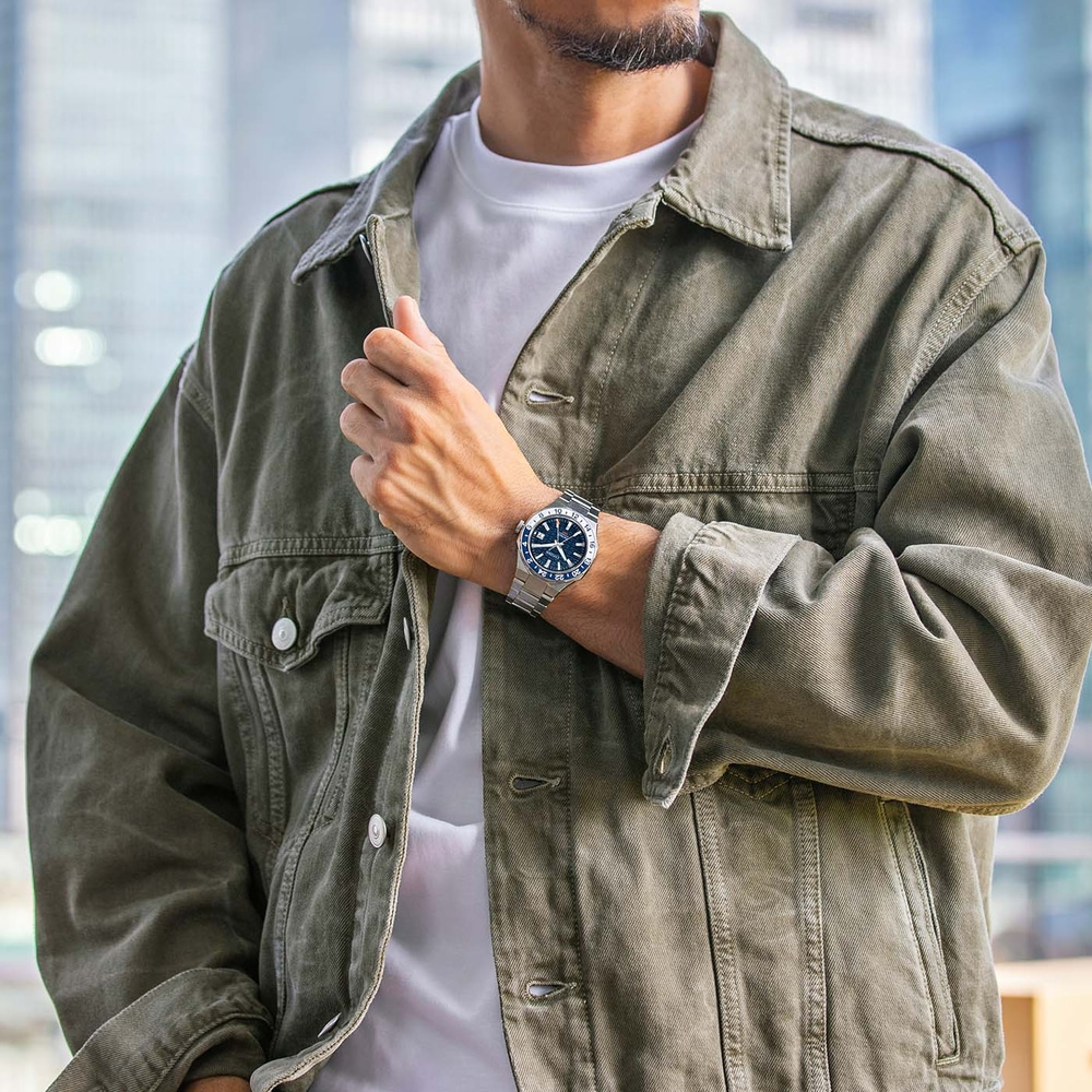 Homme portant une montre et une veste verte, posant pour une photo.