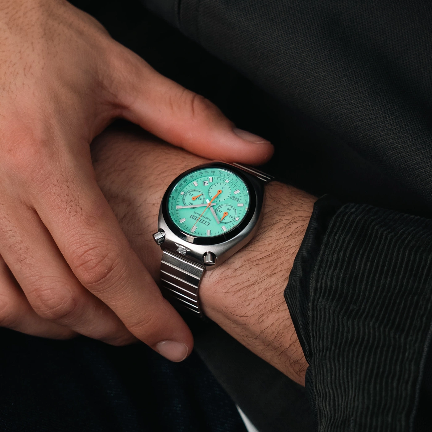 Une main porte une montre Citizen chronographe verte sur un fond sombre.
