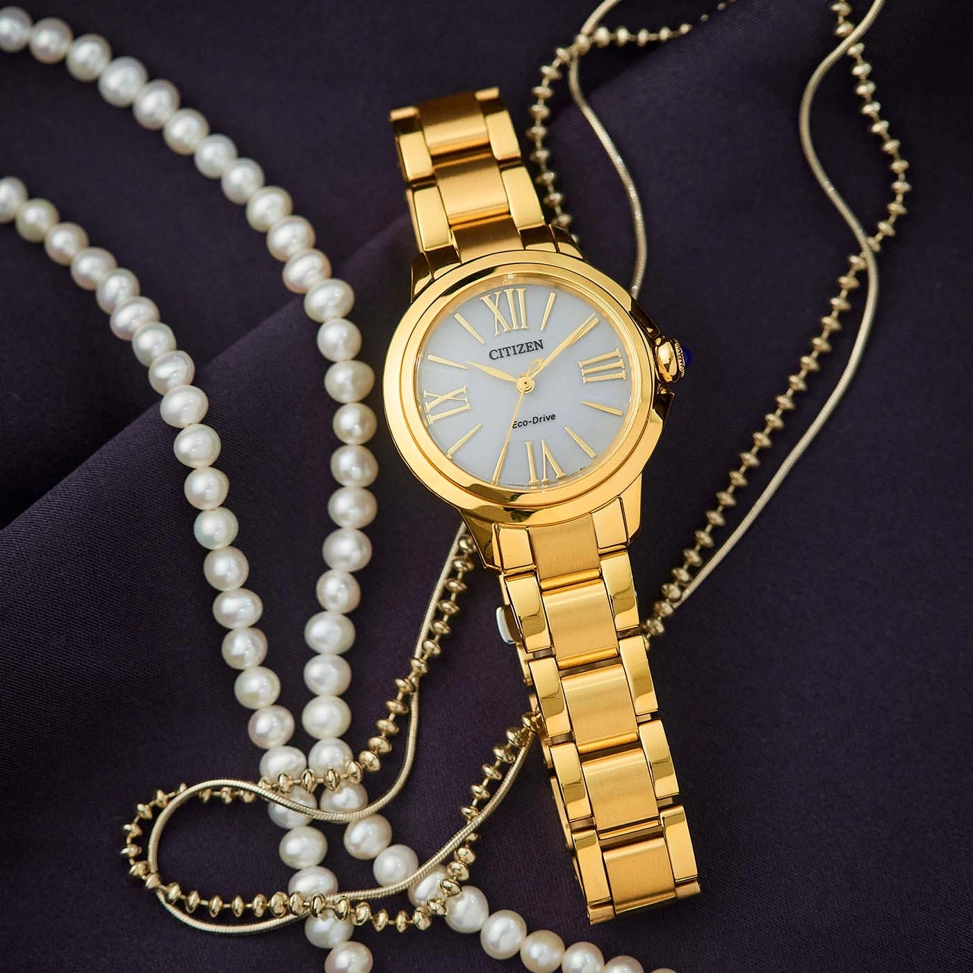 Goldene Citizen-Uhr mit Perlenkette auf dunklem Stoff.