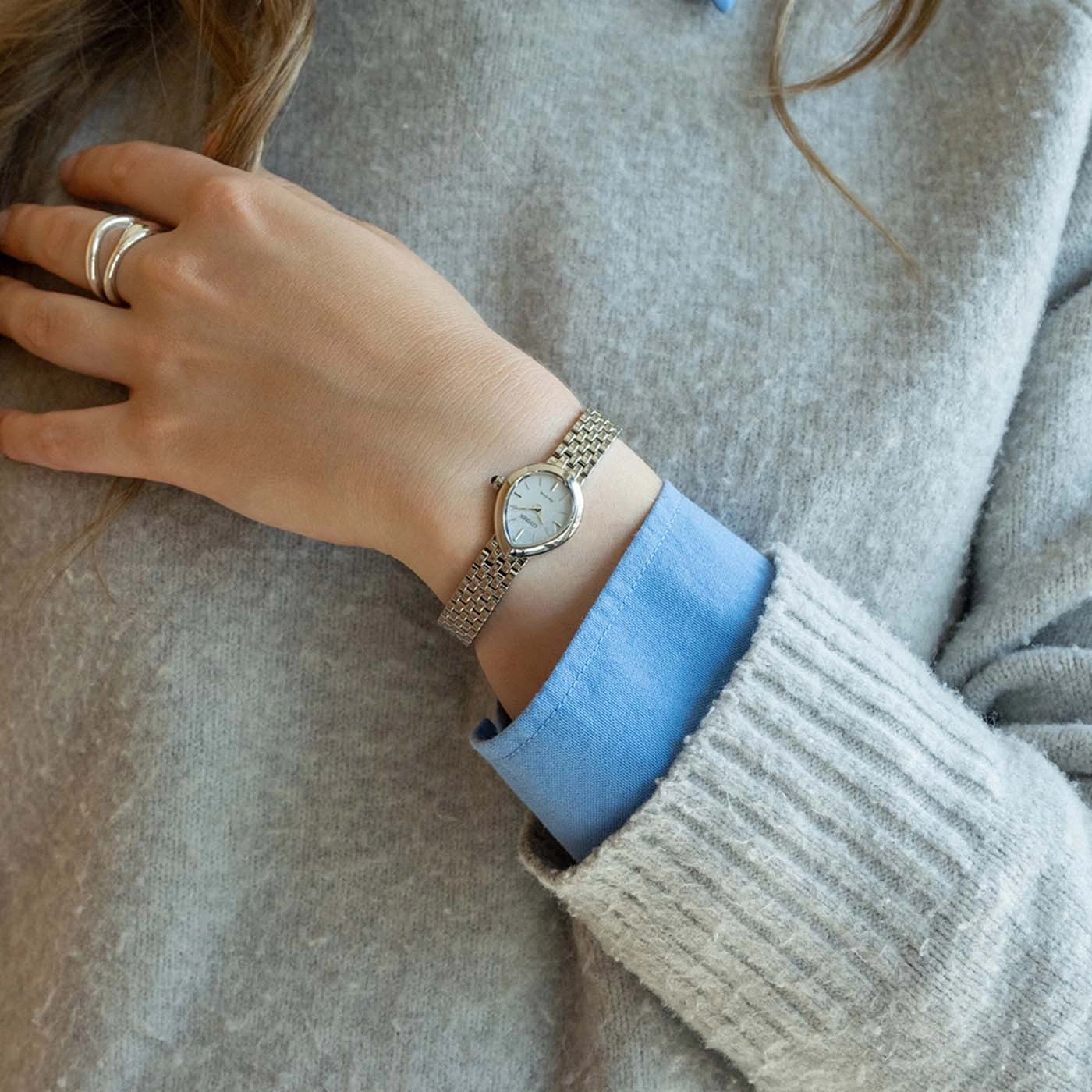 Une femme porte une montre argentée et une bague dorée sur son poignet.