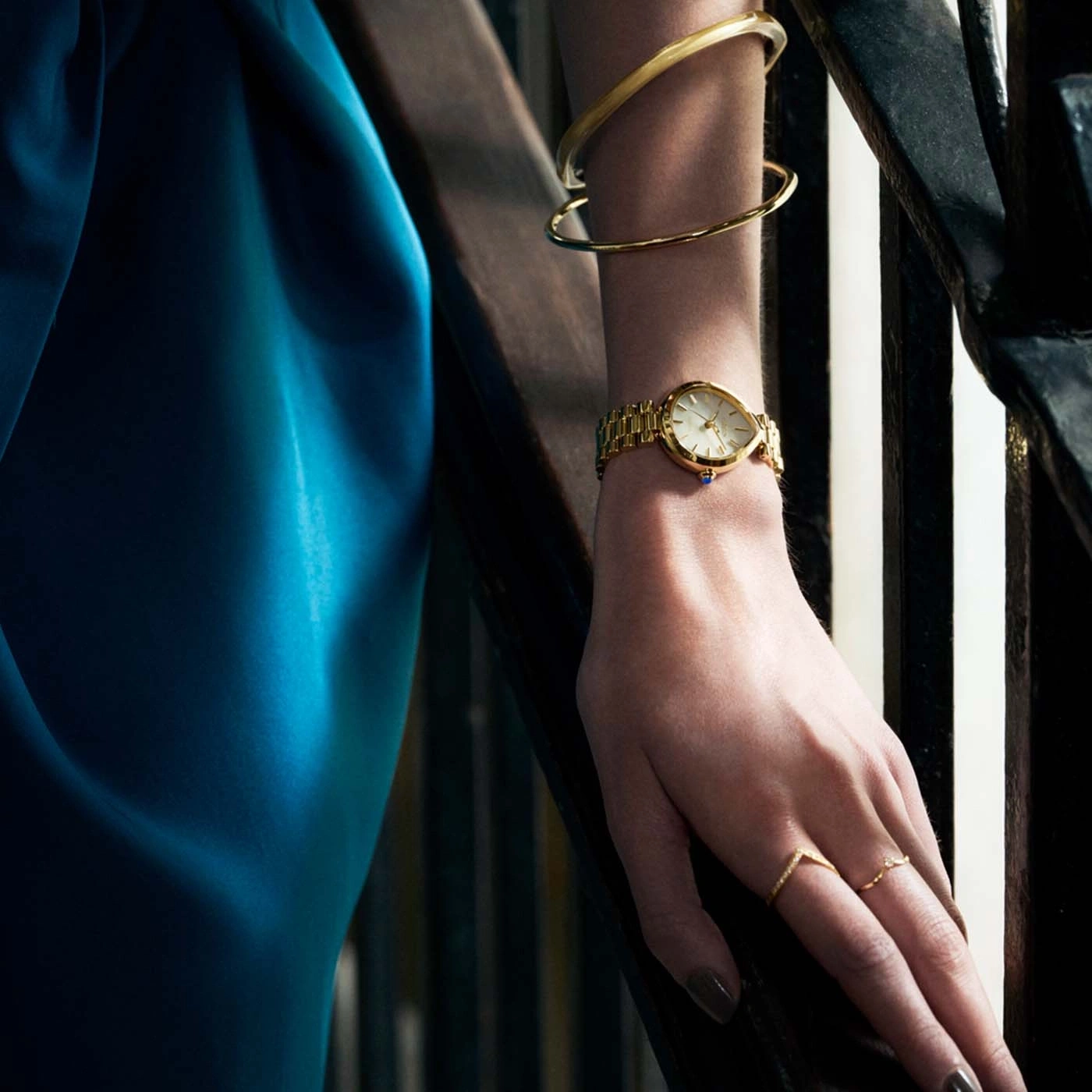 Une femme porte une robe bleue, une montre en or et des bagues.