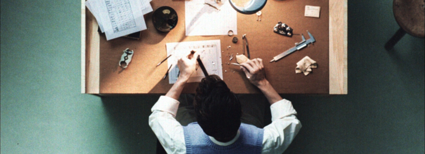 Une personne travaille sur une table avec des outils et des papiers, vue de dessus.