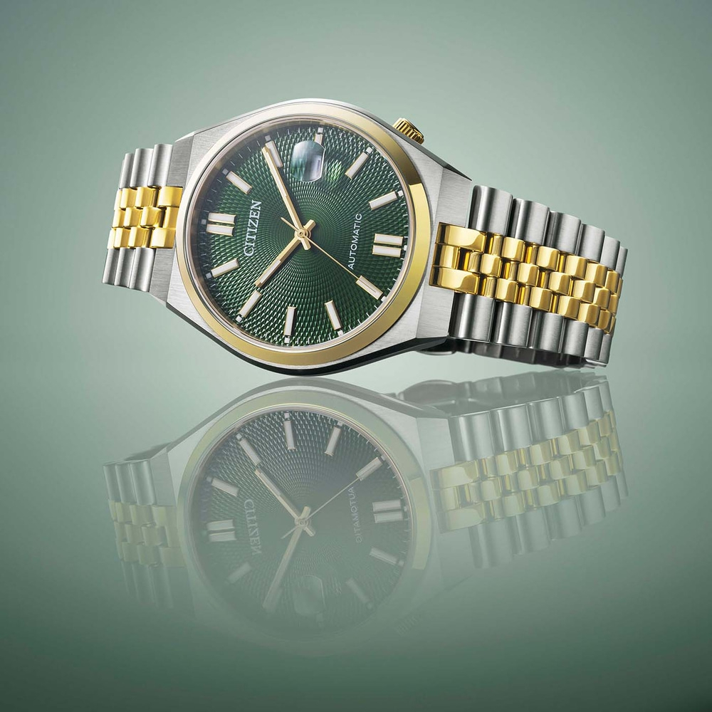 Montre Citizen avec cadran vert et bracelet or et argent, reflétée.