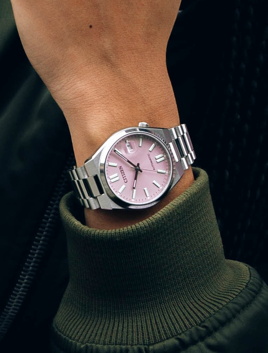 Une montre citizen automatique sur un poignet, cadran rose pâle et bracelet métallique.