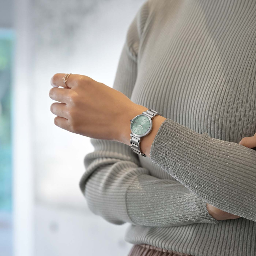 Femme portant une montre argentée au poignet gauche, un pull gris.