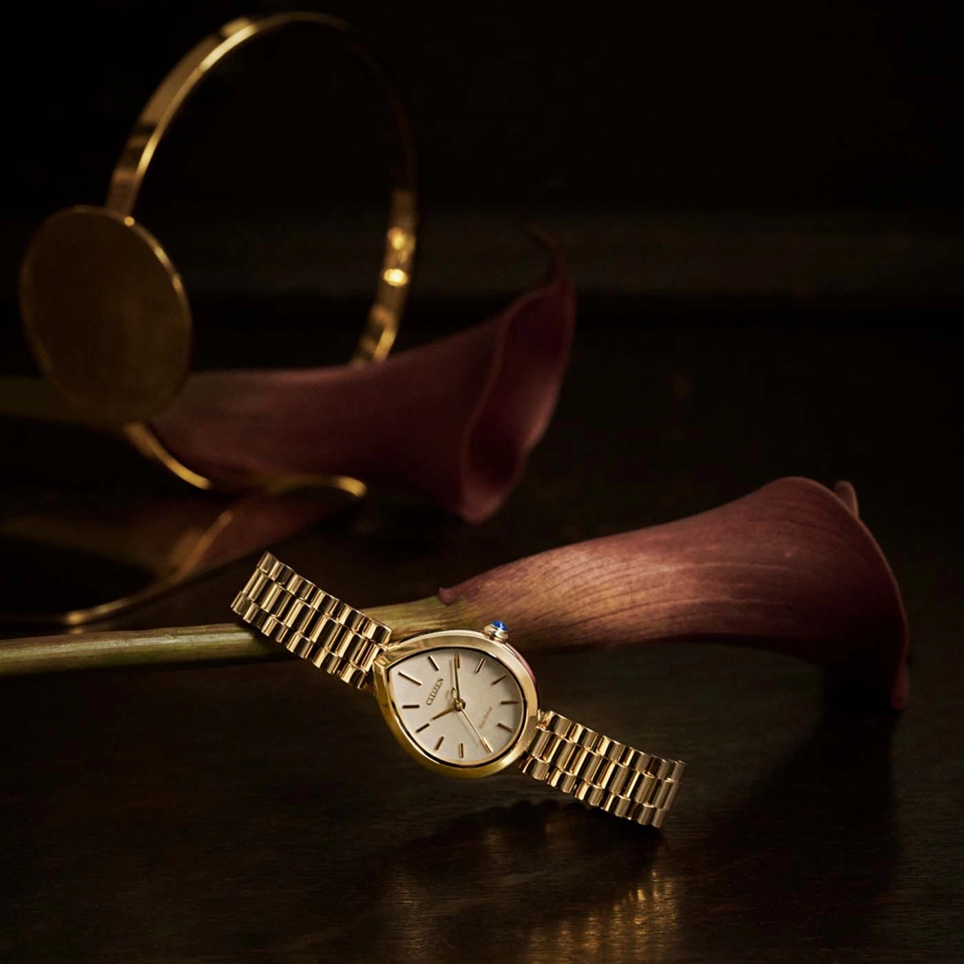 Montre bracelet dorée avec des callas et un bracelet doré.