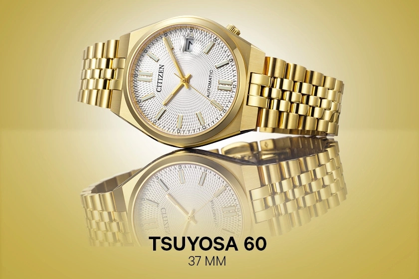Une montre Citizen TSUYOSA 60 dorée avec bracelet et cadran blanc, réfléchie sur une surface.