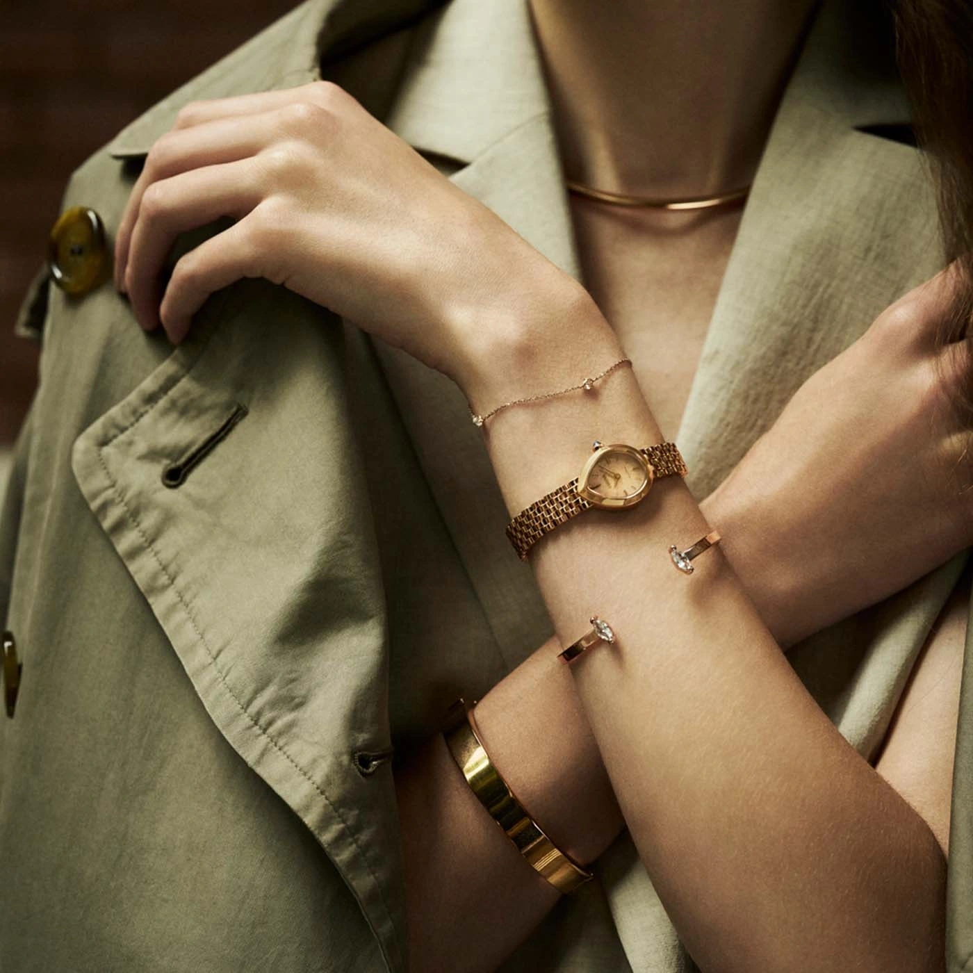 Une femme portant une veste et des bijoux en or, y compris une montre et des bracelets.