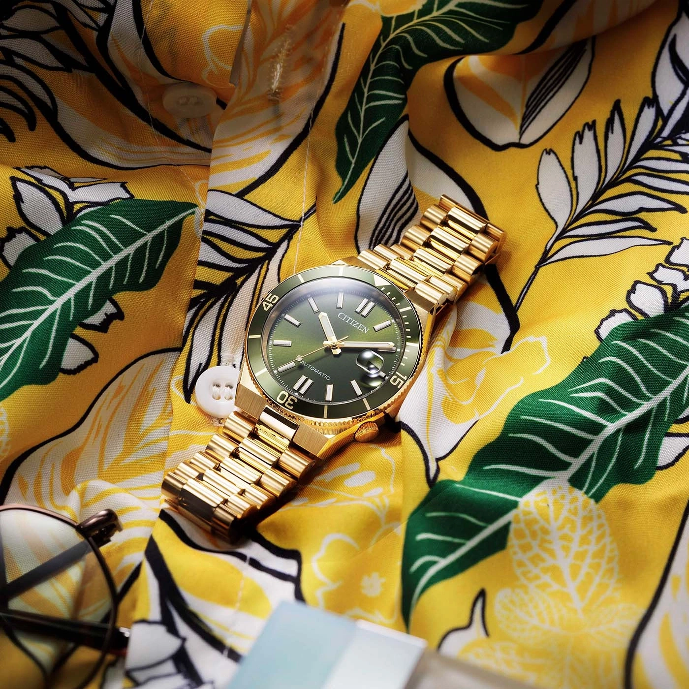 Une montre dorée CITIZEN sur une chemise jaune à motifs tropicaux.