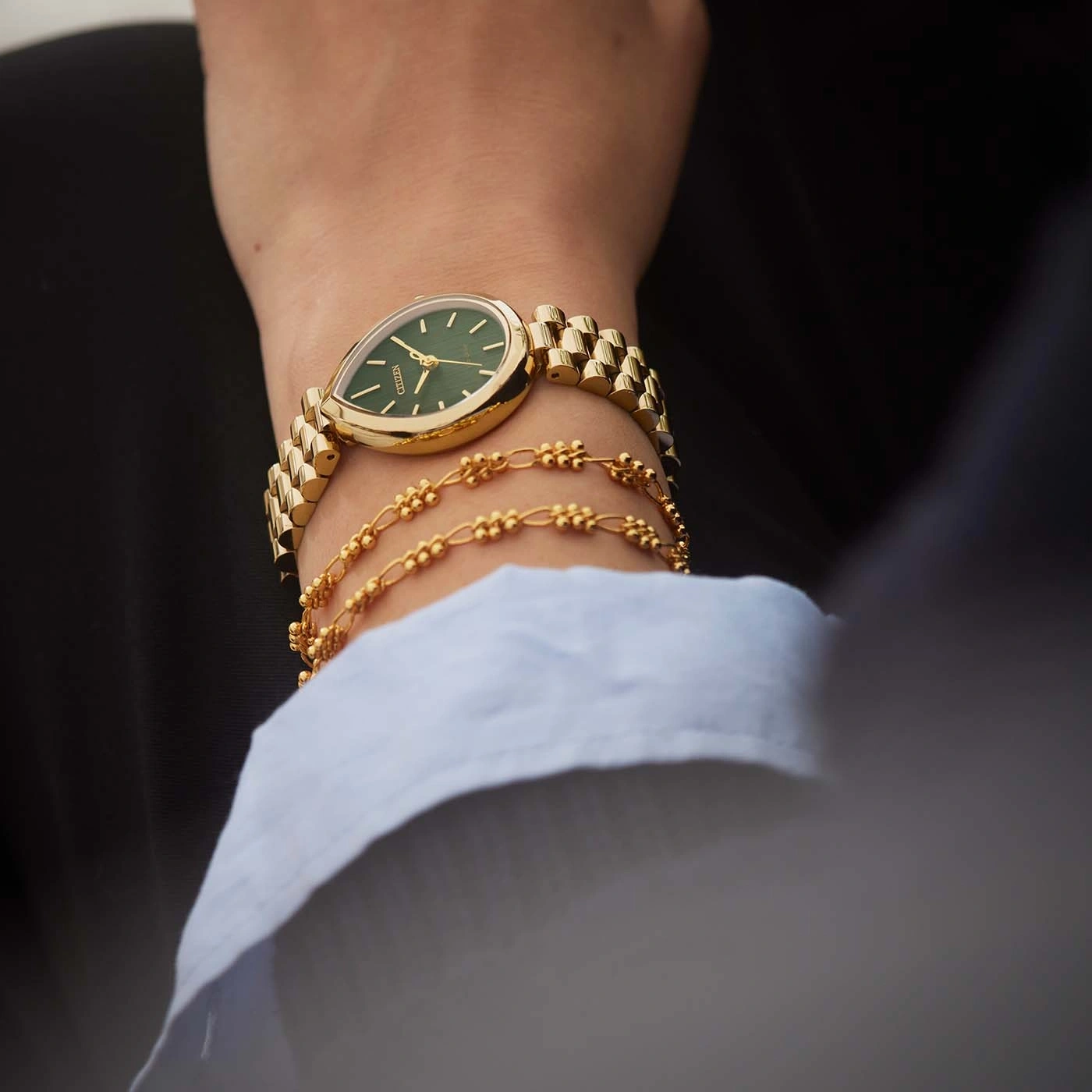 Eine Frau trägt eine goldene Uhr mit grünem Zifferblatt und passenden Armbändern.