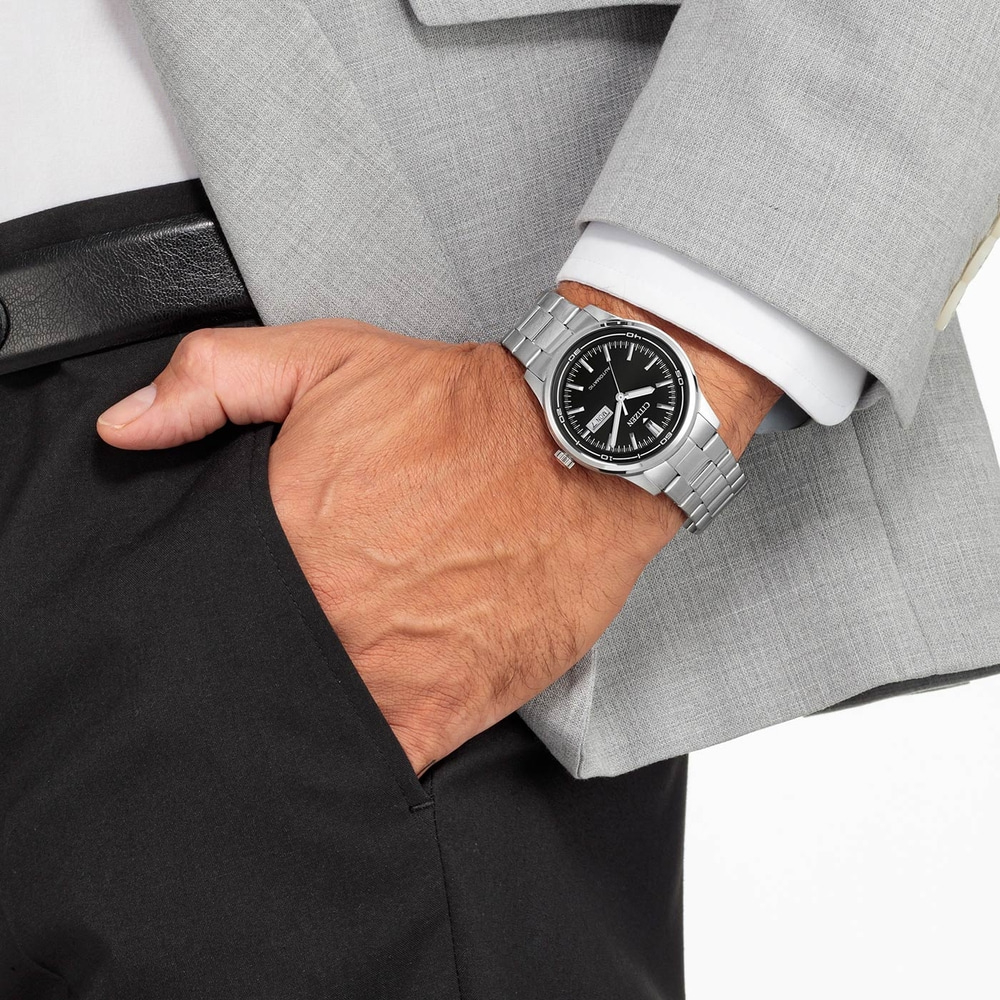 Homme portant une montre argentée, un costume et un pantalon noir, main dans la poche.