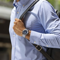 Homme portant une montre et une chemise bleue avec un sac noir sur l'épaule.