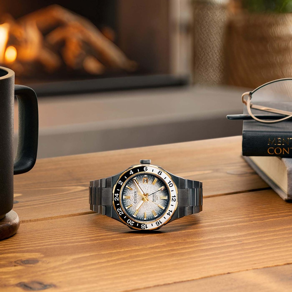Montre sur une table en bois avec une tasse, des lunettes et un livre.