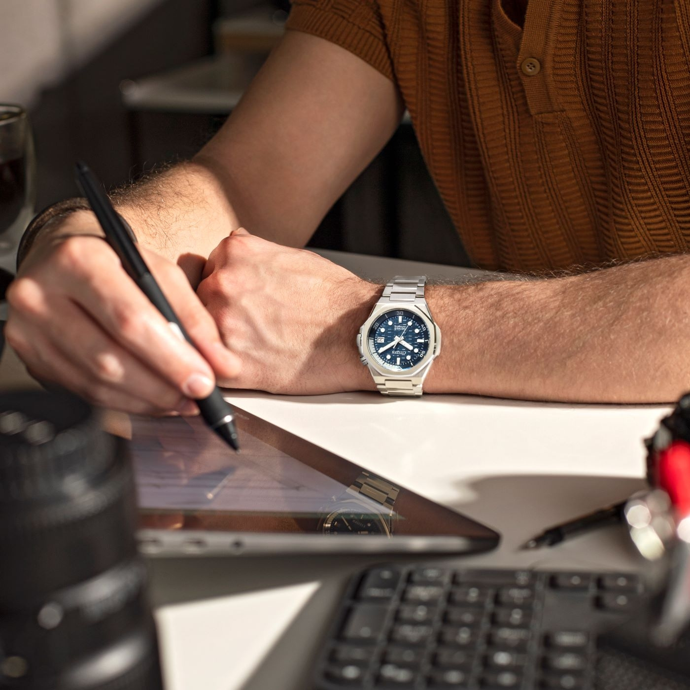 Homme travaillant sur une tablette, portant une montre et écrivant avec un stylo.