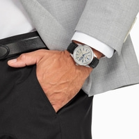 Homme portant une montre, un costume et un pantalon noir, main dans la poche.