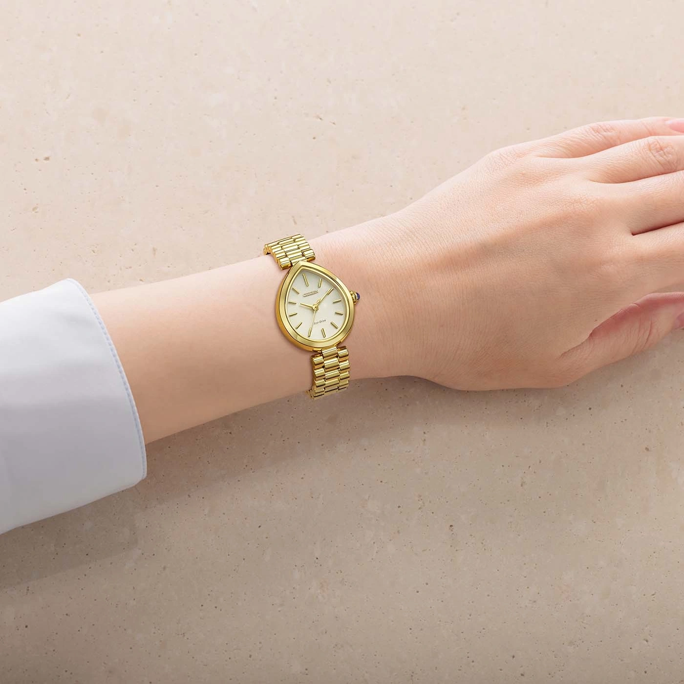 Une main portant une montre dorée élégante sur un fond texturé clair.