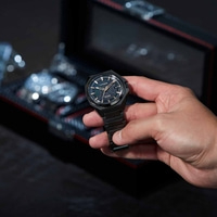 Une personne tenant une montre Citizen noire sur fond sombre.
