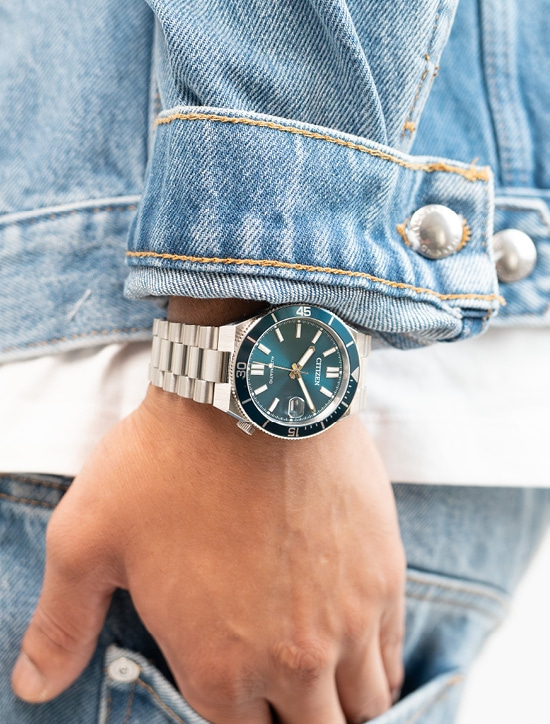 Une montre Citizen verte sur un poignet vêtu d'un jean.