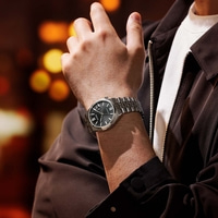 Homme portant une montre argentée avec un cadran noir et une veste marron.