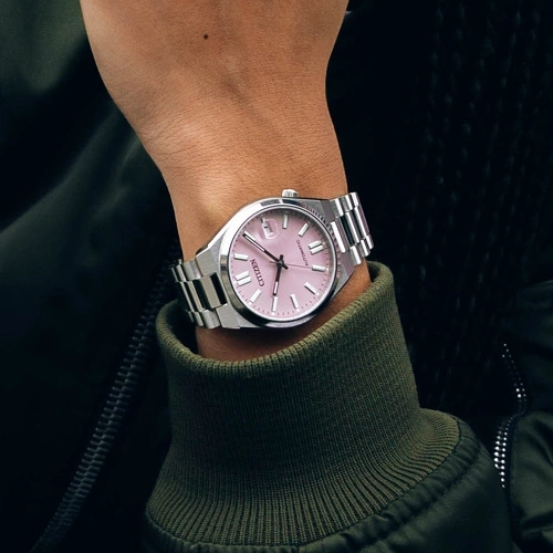 Montre Citizen rose sur un poignet, avec une veste verte.