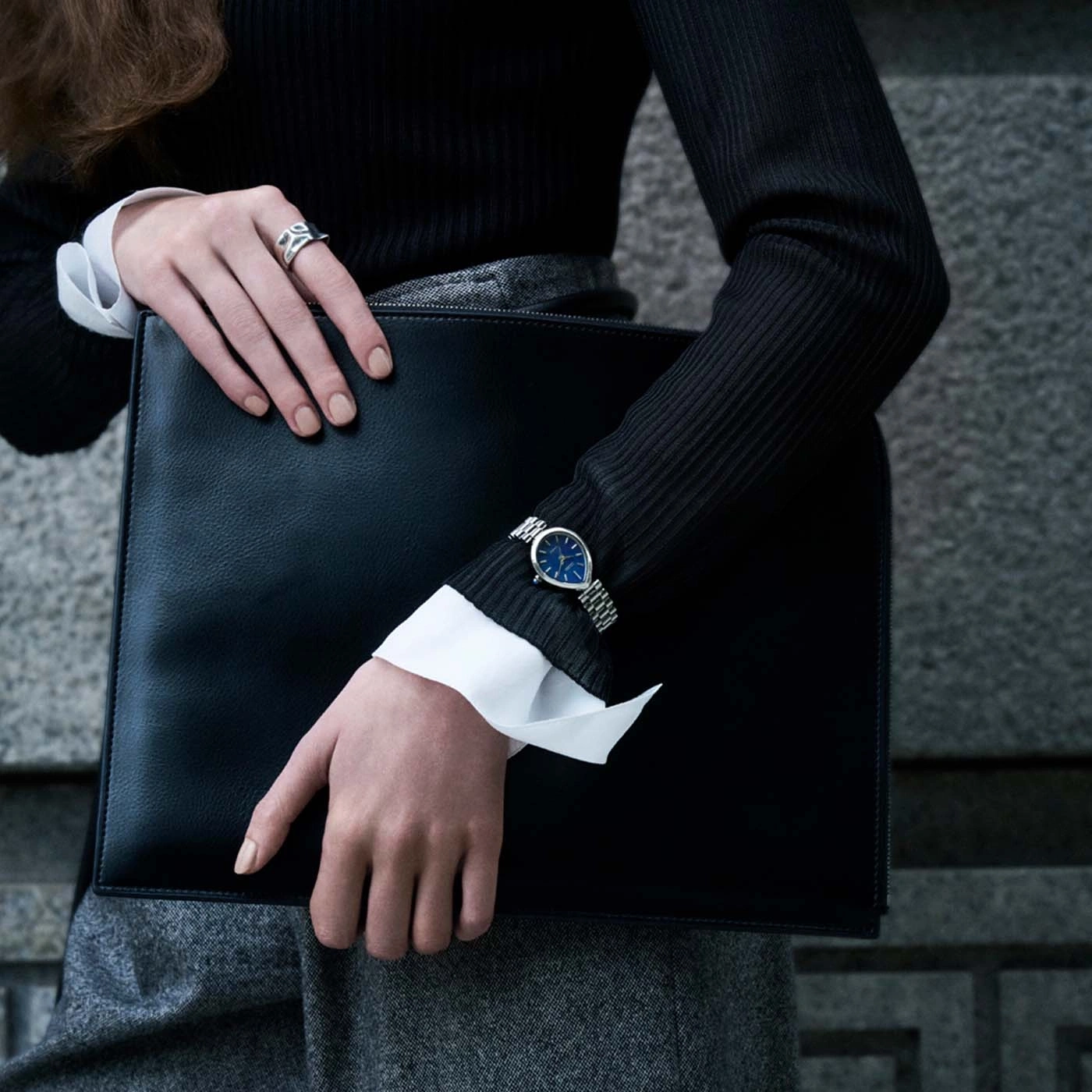 Frau hält ein schwarzes Portfolio mit einer eleganten Uhr und einem Ring.