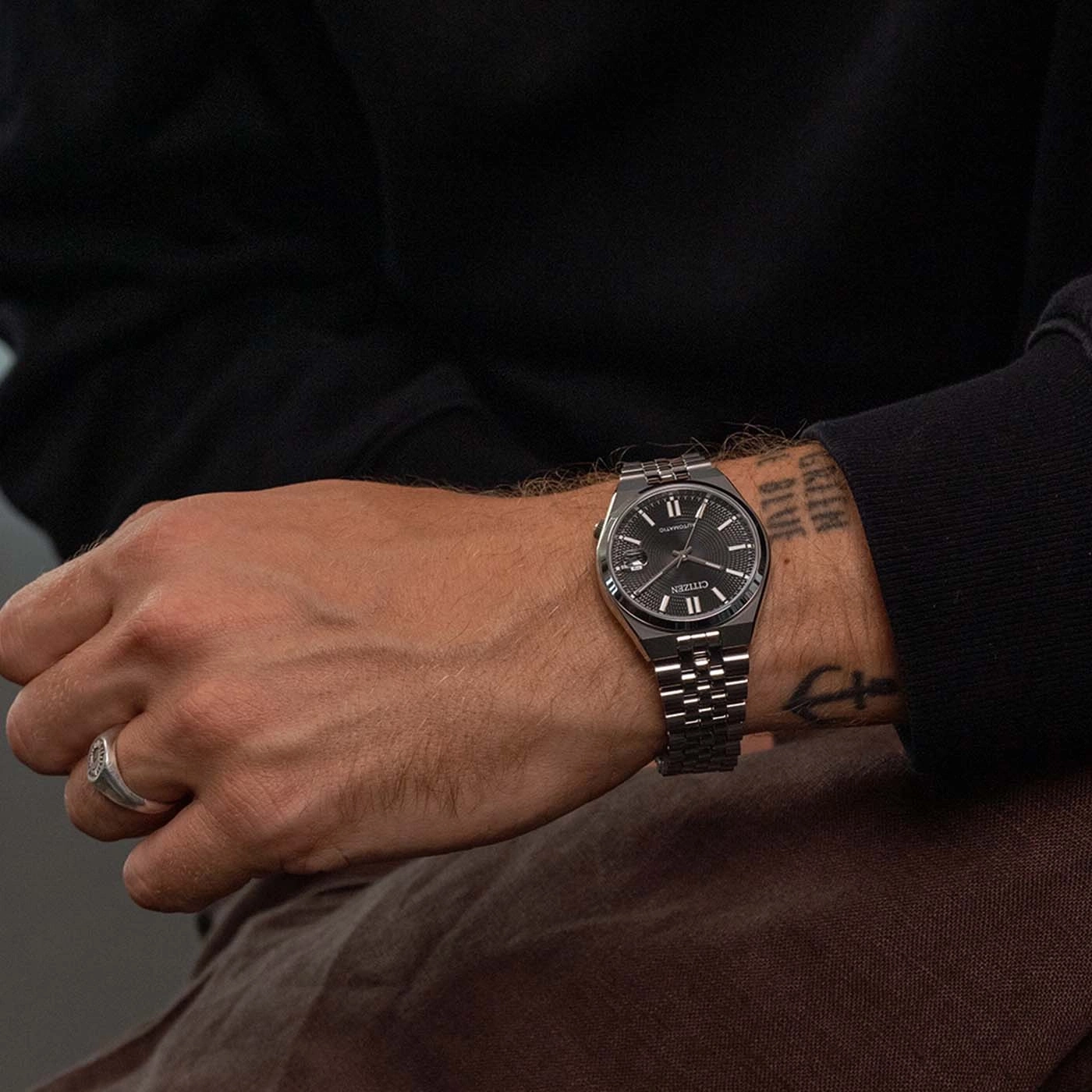 Homme portant une montre Citizen argentée avec des tatouages au poignet.