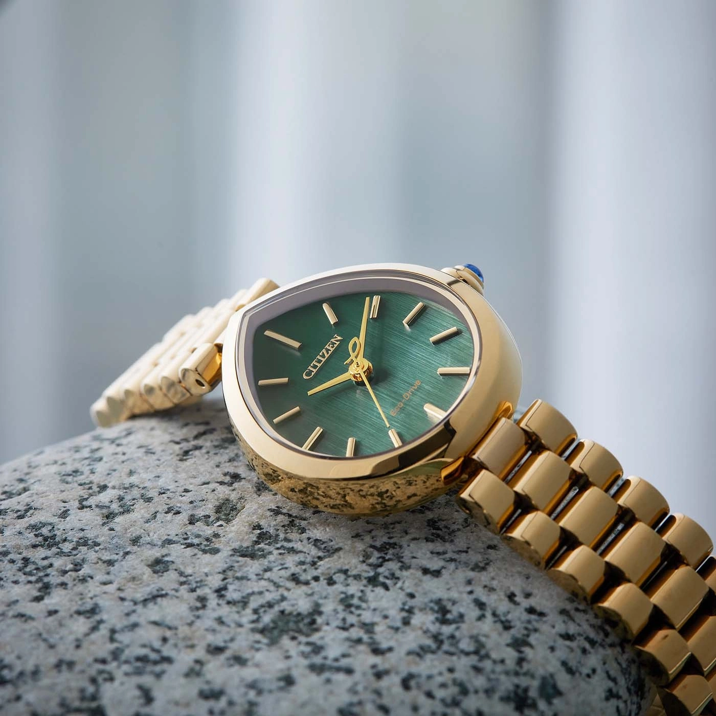 Eine goldene Citizen-Uhr mit grünem Zifferblatt auf einem Stein.