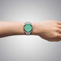 Montre Citizen verte avec bracelet métallique portée au poignet gauche.