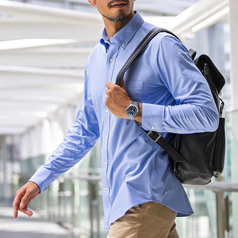 Homme en chemise bleue avec montre et sac à dos marchant dans un bâtiment