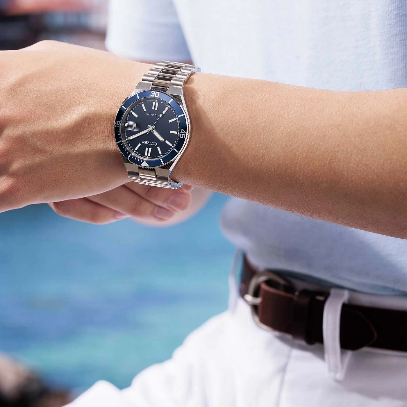 Une montre Citizen argentée sur un poignet, avec un fond bleu flou.