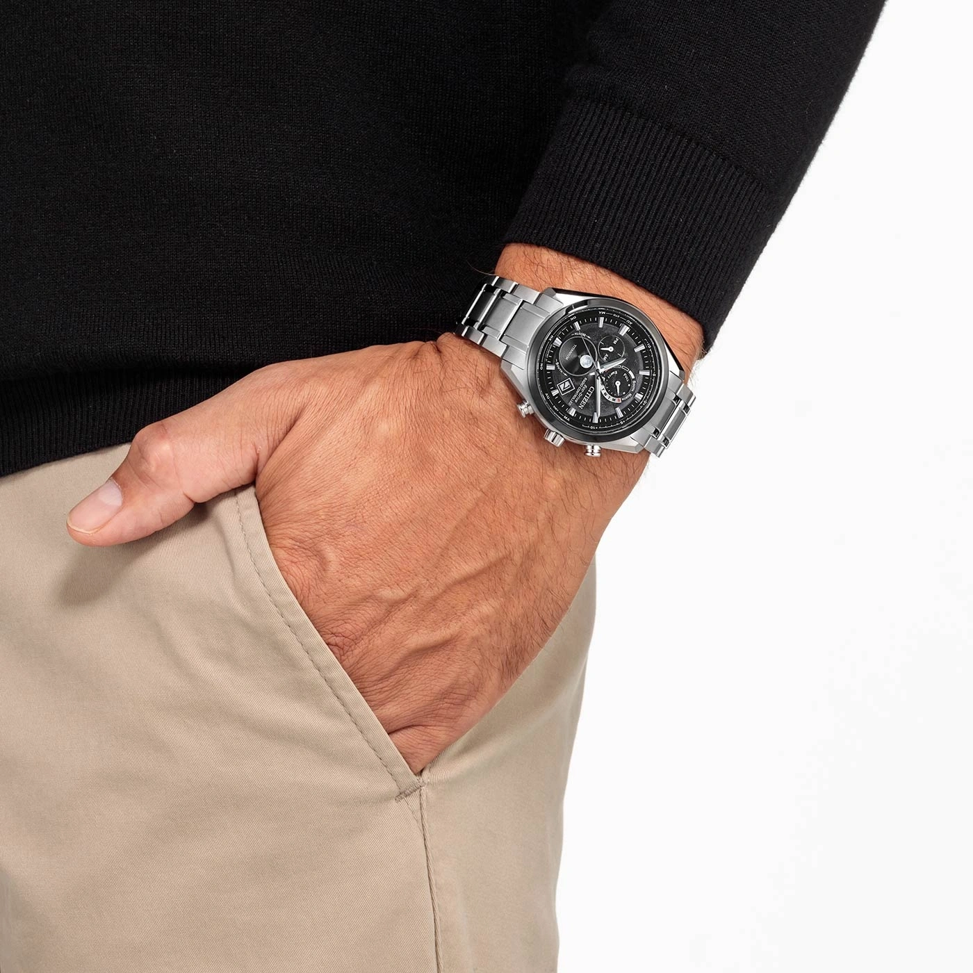 Homme portant une montre argentée et un pull noir, le reste dans un pantalon beige.