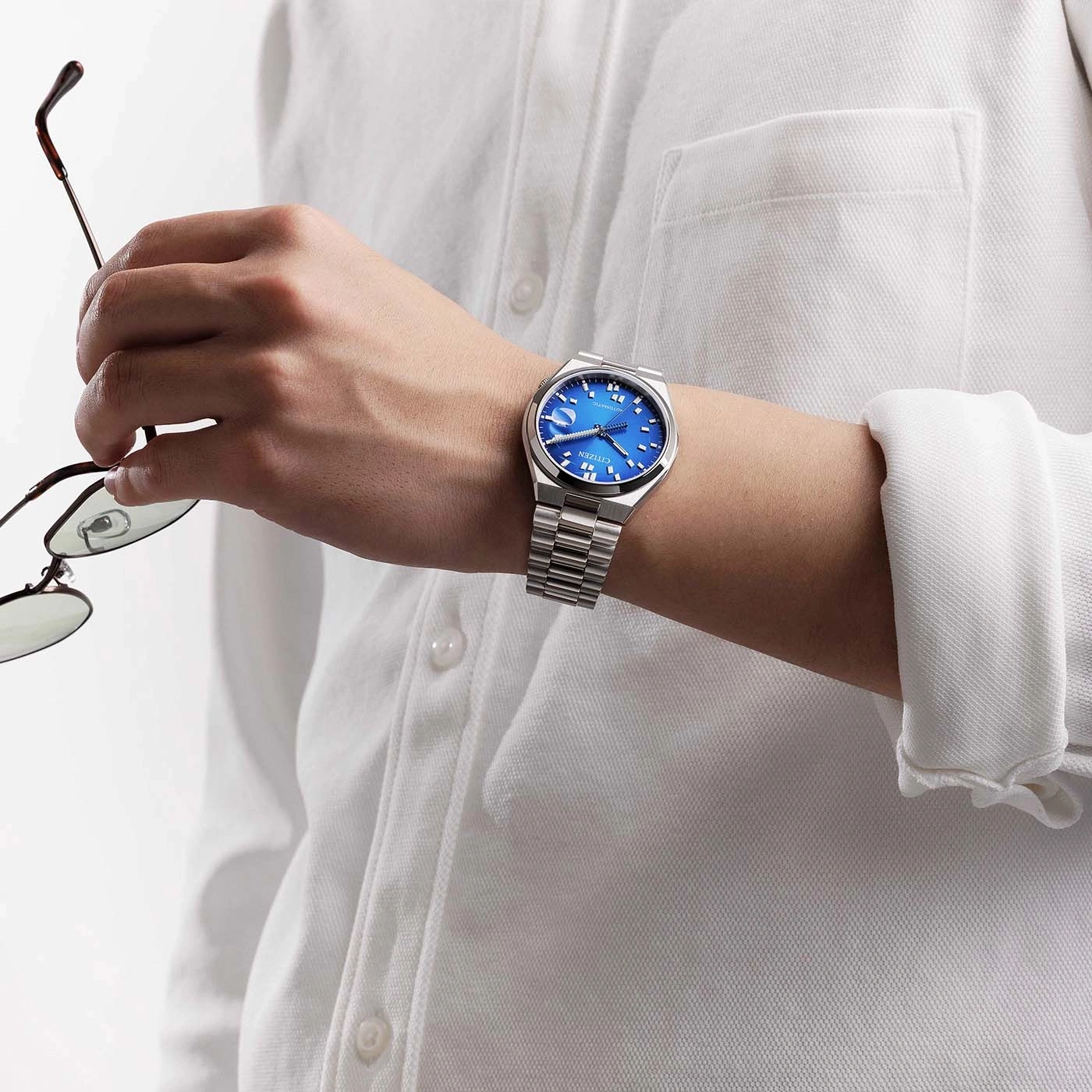Homme tenant des lunettes, portant une montre Citizen bleue sur un polo blanc.