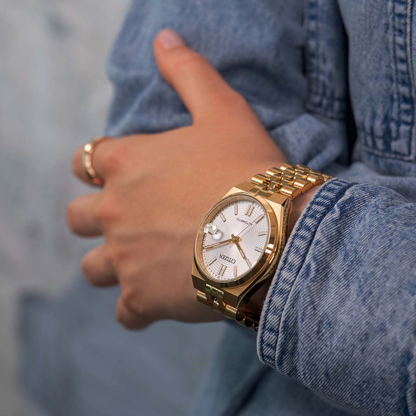 Une femme porte une montre dorée Citizen sur un bracelet en jean.