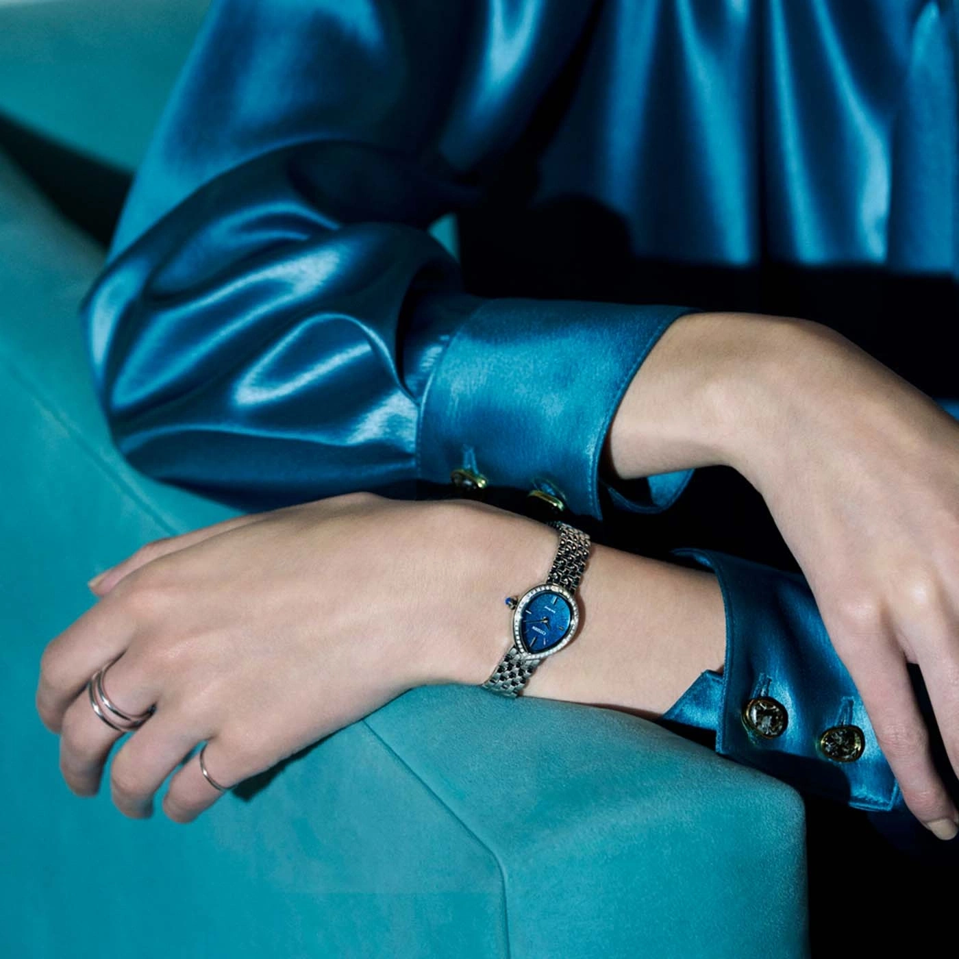 Eine Frau trägt ein blaues Satin-Kleid mit einer Uhr am Handgelenk.