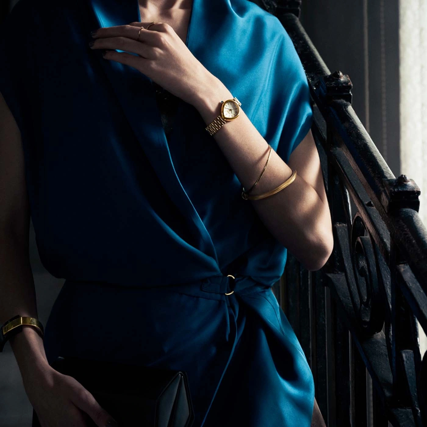 Femme en robe bleue avec une montre dorée et un bracelet.
