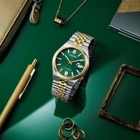 Montre Citizen avec cadran vert, bracelet or et argent, sur surface verte avec accessoires.