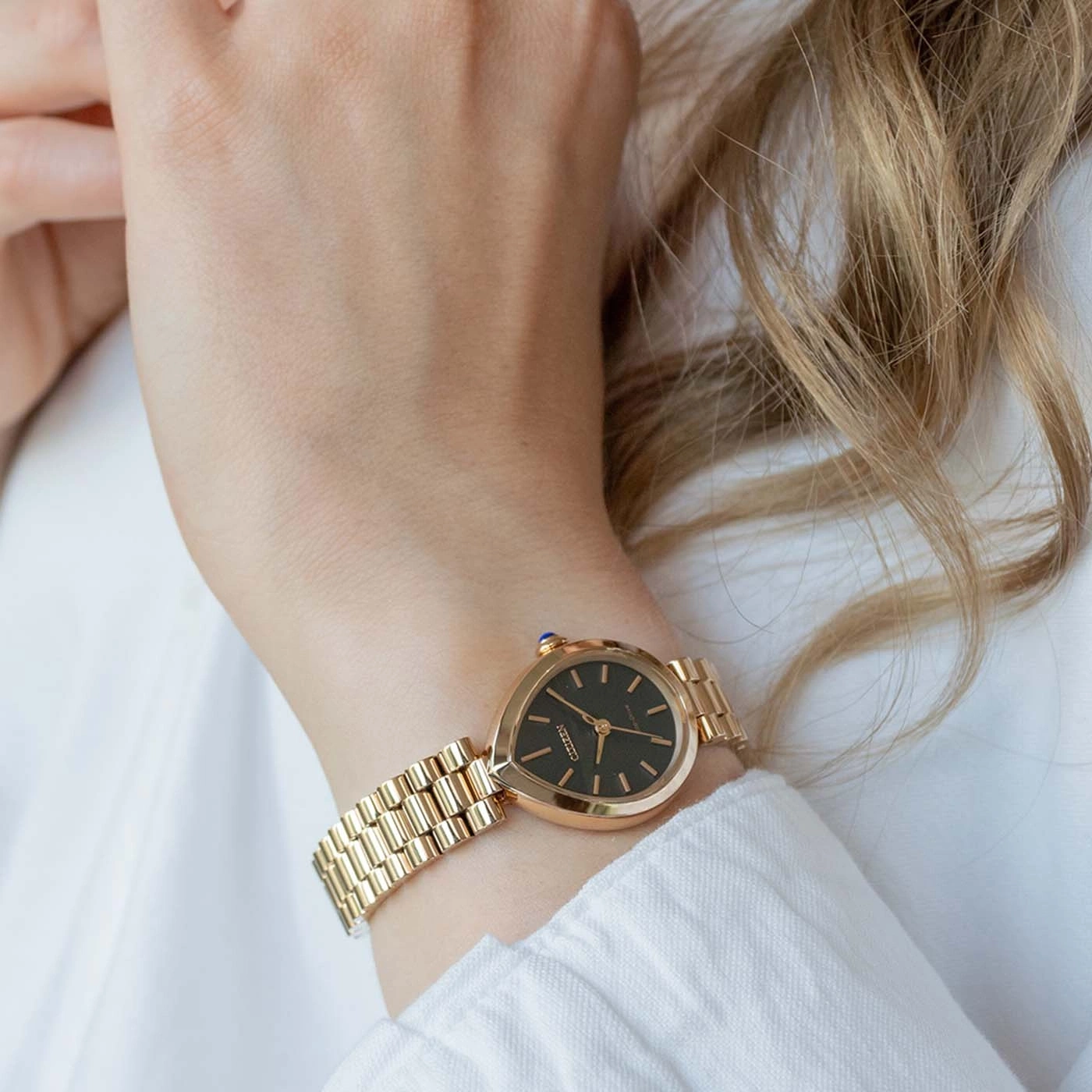 Eine Frau trägt eine goldene Uhr am linken Handgelenk, bekleidet mit einem weißen Hemd.