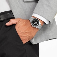 Homme portant une montre argentée, un costume et un pantalon noir, main dans la poche.