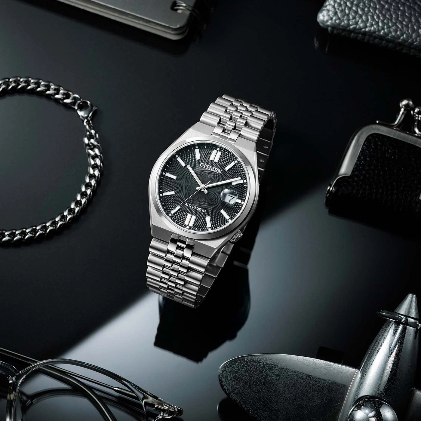 Citizen horloge met zilveren band op zwarte achtergrond, omringd door accessoires.
