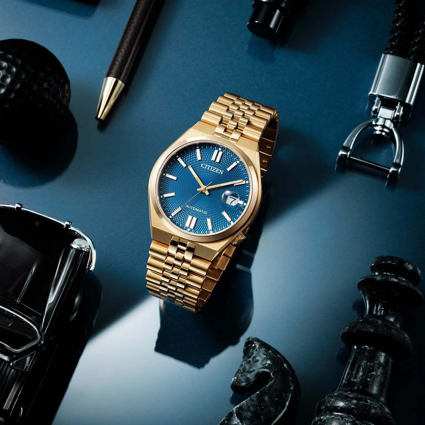 Gouden Citizen horloge op blauwe achtergrond met vrijetijdsaccessoires.